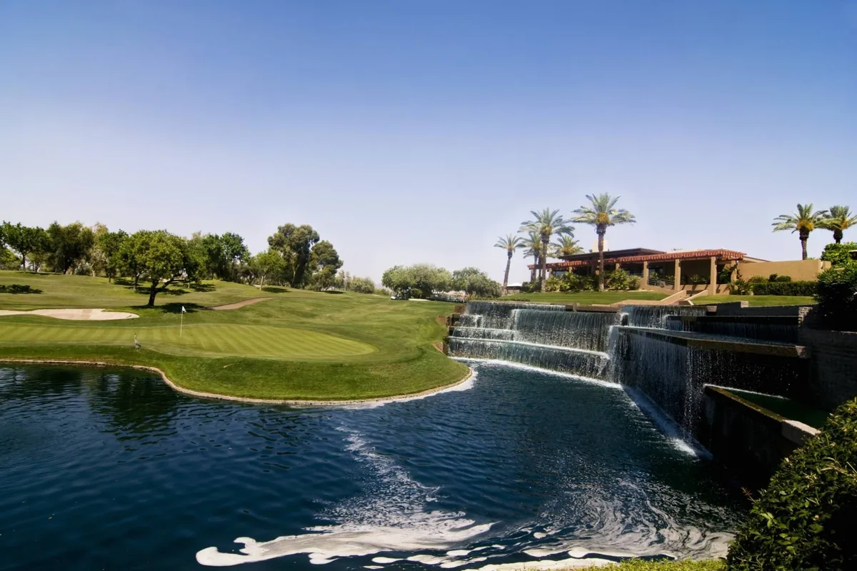 This exterior image showcases a picturesque golf course bordered by palm trees, a peaceful waterfall, and a neighboring residential building. The environment invites relaxation and outdoor enjoyment, highlighting Arizona’s unique combination of natural and landscaped beauty.