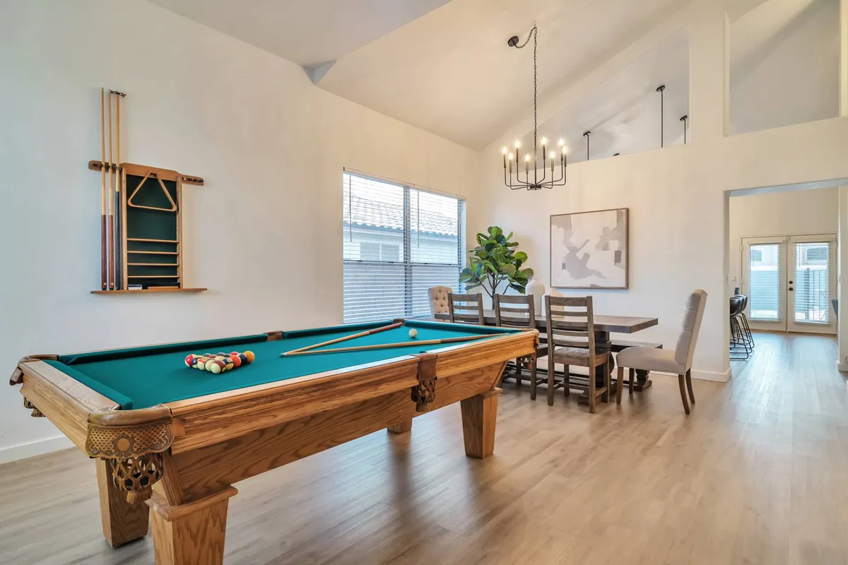 This interior image captures a vibrant scene with a pool table as the main focal point, accompanied by a spacious dining table nearby under a stylish chandelier. The room also features lush green plants, creating a welcoming and lively atmosphere ideal for both games and shared meals.