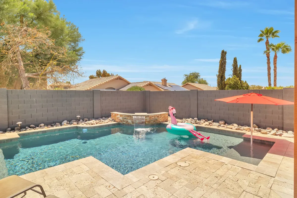 A vibrant poolside view where a pink flamingo float bobs in the water, complemented by a stone water feature and an outdoor umbrella for shade. The scene radiates playfulness and tranquility, inviting guests to imagine sunny days spent swimming or lounging poolside with friends and family.