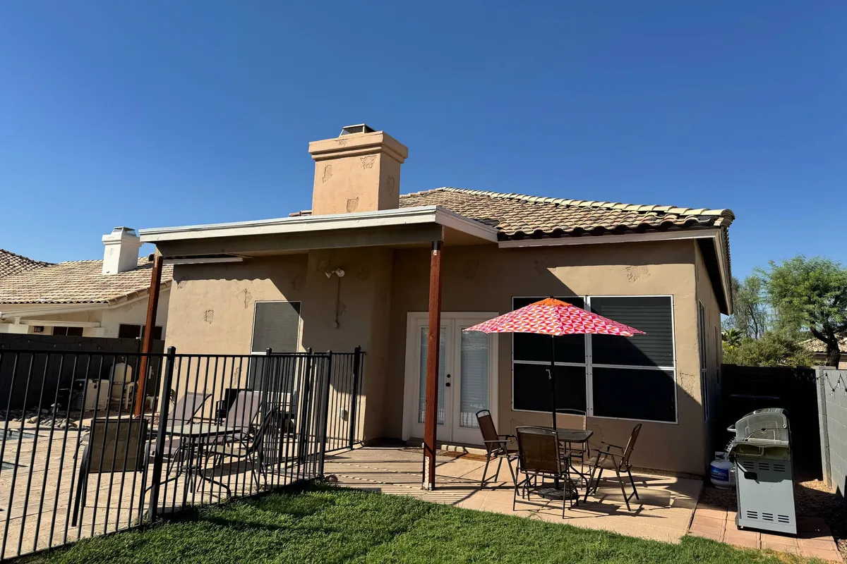 A cheerful outdoor space with a colorful patio umbrella, comfortable seating, and a view of the house's facade. The setup is perfect for group gatherings, outdoor dining, or casual conversations in the sun, reinforcing the sense of togetherness and celebration with friends or family.
