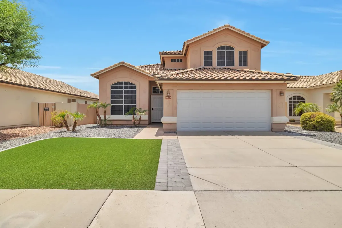 The image showcases the home's inviting front entrance, large windows, landscaped lawn, and a spacious driveway and garage. The scene suggests a welcoming arrival for groups and plenty of space for activities like outdoor barbecues, welcoming pets, or just enjoying the neighborhood vibe.