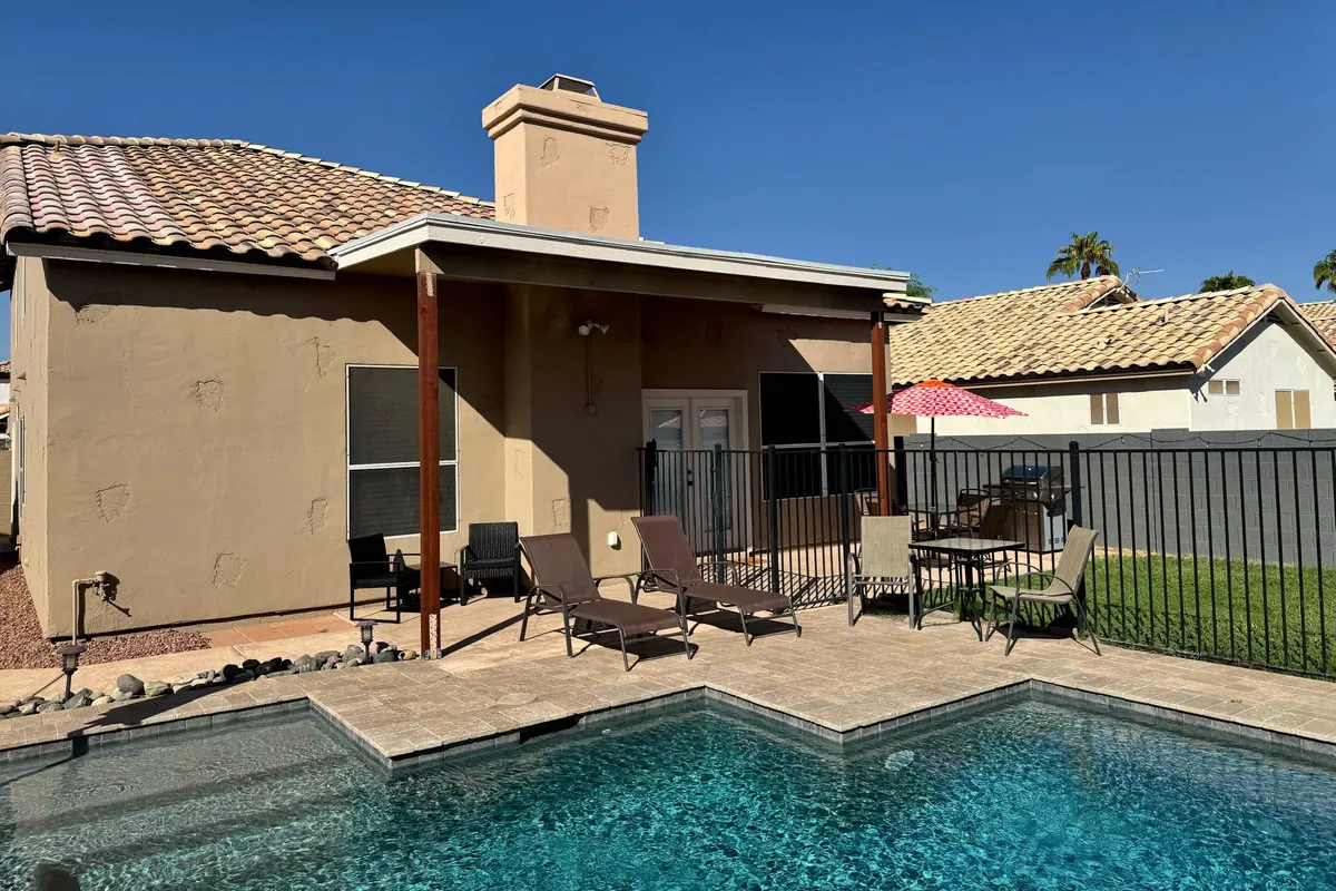 This image features a sparkling swimming pool surrounded by lounge chairs and an outdoor dining area. The setting is ideal for sunbathing, swimming, and group meals, embodying a relaxed and sociable atmosphere. The pool is the highlight, inviting guests to unwind and socialize in the Arizona sunshine.